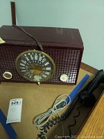 Front view of vintage Philco radio showing circular AM dial, chocolate-brown exterior, power cord, and a black handset with coiled cord.