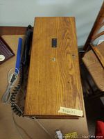 Top view of the rectangular wooden box housing the phone's internal components, showing natural wood grain and some scuffs.