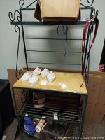 Full view of metal bakers rack with wood middle shelf, showing bottom metal wire shelves and items placed on the wood shelf.
