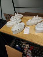 Overview of 5 white milk glass boat-shaped trinket boxes placed on wooden surface.