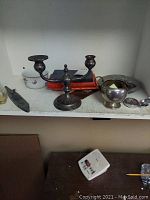 Shelf display featuring sterling silver creamer, three-arm candle holder, books, and small containers