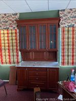 Full view of cherry wood hutch with glass-paneled upper cabinet, marble top and base cabinet with drawers and doors.