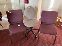 Three office chairs placed side by side; one gray office chair with wheels in middle flanked by two maroon fabric office chairs with metal legs.