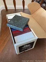 Box and samples showing one dark blue/green quartz sample resting on the box lid, multiple other samples visible inside box.