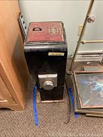Full view of the tall vintage Hobart coffee grinder showing black and red metal body with handle on top lid.