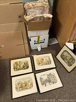 Photo showing five vintage framed prints laid on carpeted floor near boxes and packing materials. Prints show early America scenes with some dirt and wear on frames and mats.