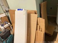 Stack of various sizes of flattened cardboard shipping boxes and white foam packaging pieces leaning against the wall.