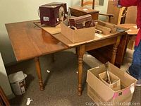 Full view of cherry drop leaf table with some scratch marks and minor surface wear. Shows turned legs and extended leaf on one side.