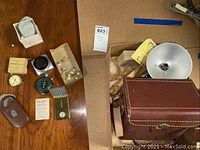 Overview of all items laid out on wood surface including Reading Railroad buttons, boxes, watches, and camera accessories.