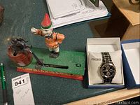Photo showing the reproduction mechanical coin bank with a figure and the Seiko watch in box on a table.