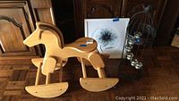 Wooden rocking horse, floral print in frame, birdcage candle holder arranged side by side against wooden cabinet