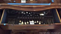 Drawer with full set of forks, spoons, and knives with polished stainless steel heads and gold-tone decorative handles arranged neatly.