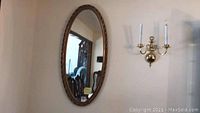 Oval wall mirror hanging on wall showing full mirror reflection and part of dining room chairs.
