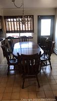 Full view of wood dining table set with chairs in kitchen area, showing table and six chairs under chandelier lighting.