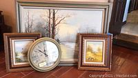 All three framed art pieces and the round clock arranged on floor against a wall, showing size and appearance.