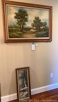 Large framed landscape painting on wall showing a country path and houses with trees, signed Louis M. Cavetello.