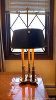 Photo of Stiffel bedside lamp on a table near window, displaying black shade and triple candle-like gold-tone base