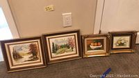 Three framed paintings on floor: one original Monica Marshall landscape painting and two smaller unsigned paintings in ornate frames.