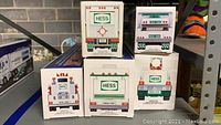 Front view of the collection of five Hess trucks in original boxes stacked on a grey metal shelving unit. Boxes show clear Hess branding and years of trucks: 1988, 1992, 1996, 1998, 2000. All trucks appear unused inside boxes.
