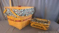 Two Longaberger baskets with holly berry pattern liners and wooden lid on larger basket, wooden swinging handles visible on both.