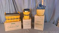Three Longaberger baskets displayed on top of their collector club boxes against a curtain background.