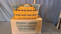 Full view of the basket on top of the original box showing the basket's plaid fabric liner and wooden handle.