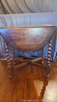 Photo of the antique solid wood drop leaf table with leaves down showing dark finish and spindle legs.