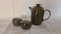 Brown Denby tea pot with lid, matching sugar bowl and creamer on white background.