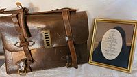 Photo showing entire leather briefcase with buckle straps alongside the framed poem.