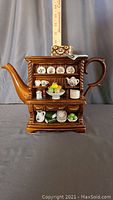 Front view of brown ceramic teapot modeled as a miniature Welsh dresser with spout and handle