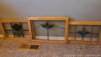 Full view of three stained glass panels laid side-by-side, wooden frames, each with different designs and two smaller pieces and one larger one.
