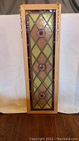 Full vertical stained glass panel in wooden frame showing overall design and attached hanging chains.