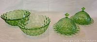 Two green depression glass bowls paired with two covered dishes with matching lids shown on white draped fabric background.