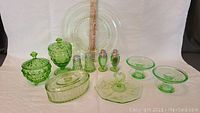 Overall grouping of all depression glass items: two salt & pepper sets, two covered candy dishes, two compote trays, relish tray, oval covered dish and 8" plate