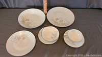 Full set of plates and bowls showing floral design and silver trim against grey background with a ruler to indicate size.