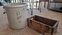 Photo of large stoneware crock and wooden crate placed on carpeted floor.