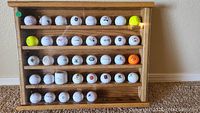 Front view of the shadow box displaying rows of assorted golf balls with logos, in wood frame behind glass.