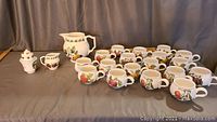 Full set displayed including all cups, saucers, pitcher, creamer, sugar bowl, and covered sugar container on gray fabric background