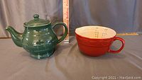 Green Longaberger pottery teapot with lid next to red measuring cup with ruler for scale.