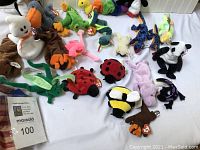 Photo showing a collection of various Beanie Babies plush toys in different animal designs and colors laid out on a white surface.