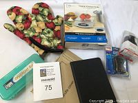 Lot items arranged on white background: two vegetable-themed pot holders, digital kitchen scale in original box, plastic organizer box, Kindle cover, and Verizon charger with packaging.