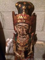Front close-up of one of the tall wooden Hindu statues showing detailed face and crown with gold and red paint accents.
