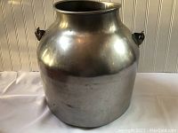 Front view of the vintage metal container showing its rounded body, narrow neck, and side handles.