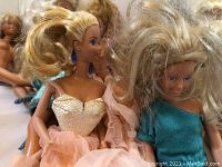 Close-up of two Barbie dolls, one in a peach dress and the other in a teal top with blue pants, showing hair and facial features.