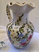 White ceramic pitcher with floral design in green, pink, and blue, ruffled top edge