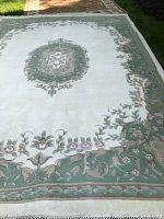 Full view of rectangular area rug laid on grass showing ivory field, central medallion, and green border with pink floral motifs