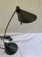 Full view of the black desk lamp showing the adjustable arm, conical shade and base, and power cord.