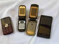 Front view of four phones side by side showing screens and keypads, including two flip phones, one slide phone, and one touchscreen phone.