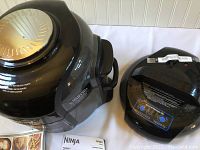 Photo of the Ninja Foodi pressure cooker main unit and crisping lid placed on a surface alongside owner's manual.