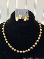 Photo of the full necklace and earrings displayed on a black velvet stand, showing the round gold-tone beads of the necklace and matching earrings.